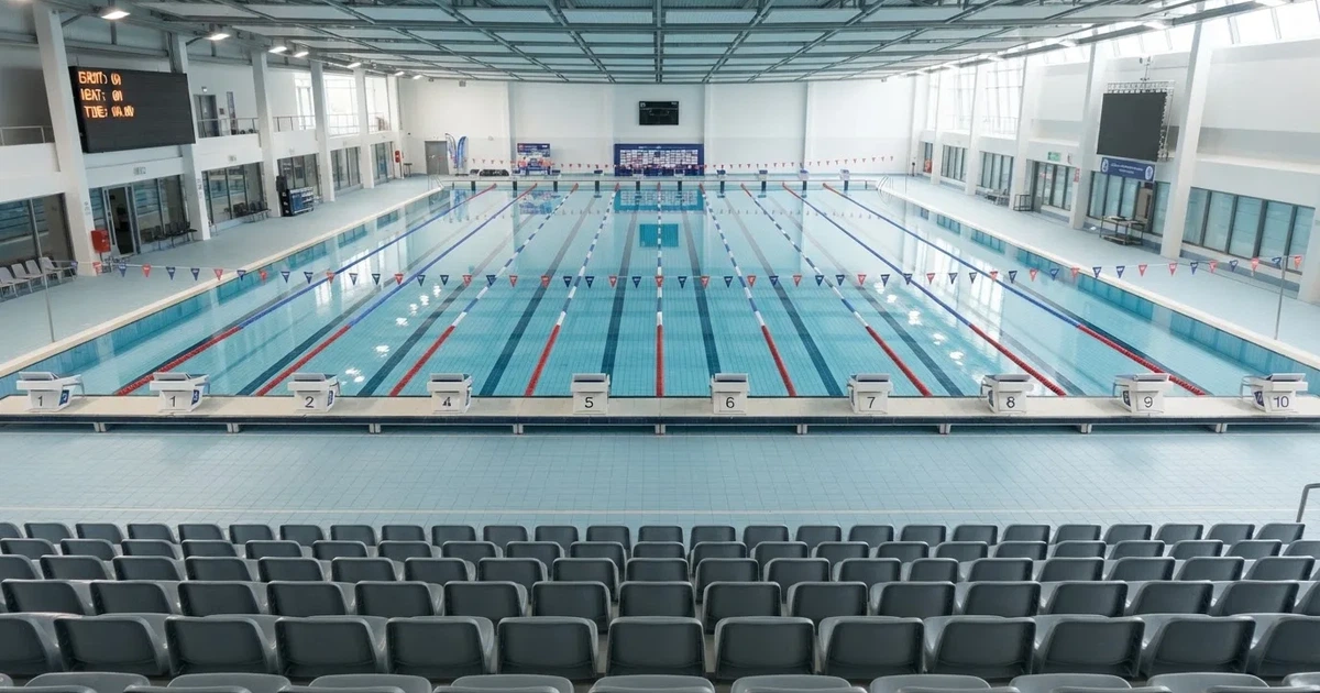 Pusty basen olimpijski z równymi torami i spokojną taflą wody, widok z trybun w jasnym świetle.