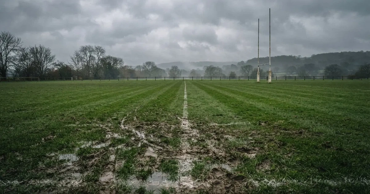 Boisko do rugby ze słupami bramki w oddali pod pochmurnym niebem, mokra trawa i ślady butów.