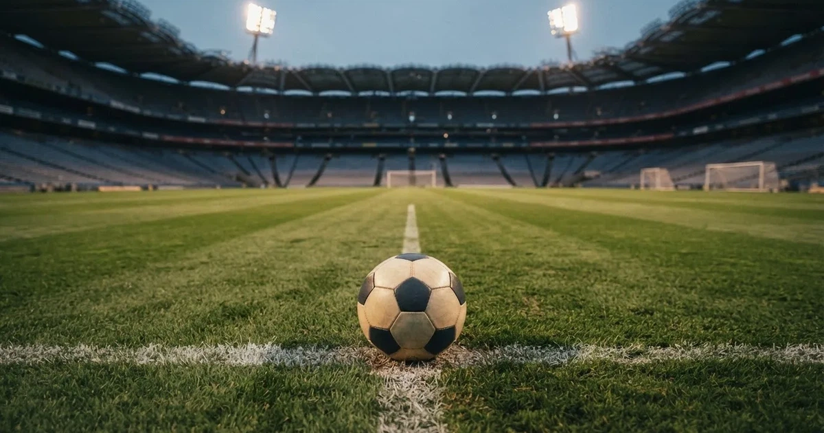 Piłka nożna leżąca na środku murawy w pustym stadionie przed meczem, rzędy siedzisk w półmroku.